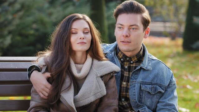 Cheerful caucasian family couple sitting in park talking friendly handsome man hug beloved woman wife discussing pleasant conversation chatter outdoors planning future journey in honeymoon together 