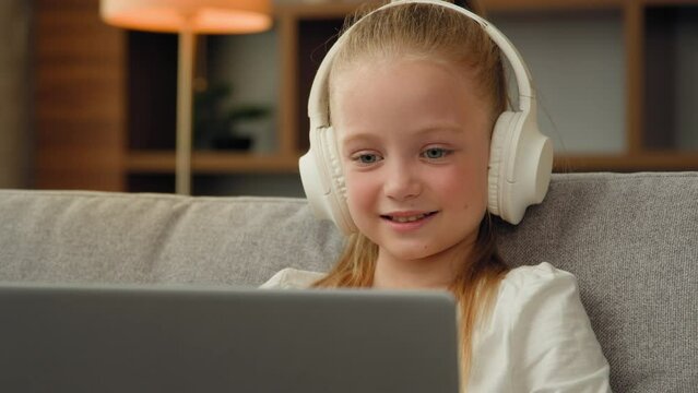 Beautiful kid child little gamer studying online on laptop at home listen audio music in headphones playing computer game laughing pretty girl watch funny cartoons use electronic device resting alone