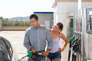 Couple standing at petrol filling station, holding fuel nozzle and refuelling their car
