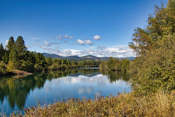 On a sunny Autumn day in Idaho, a peaceful river with a glassy surface reflects the sky and surrounding mountainous landscape.