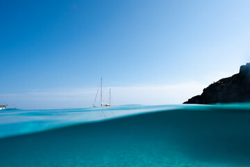 Superficie de mar mediterraneo con barco velero de fondo y cielo azul 