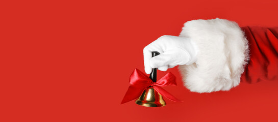 Hand of Santa Claus holding Christmas bell on red background with space for text