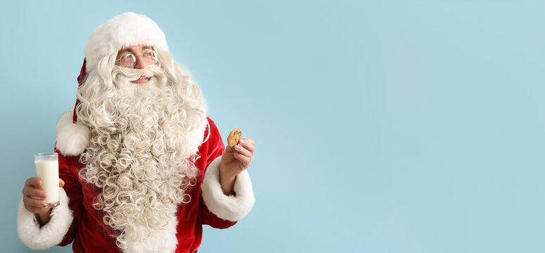 Santa Claus holding tasty cookie and glass of milk on light blue background with space for text