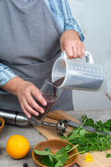 woman pours prepared healthy detox drink in a blender into a glass - a green smoothie with fresh fruits, blueberries, green spinach and kiwi.