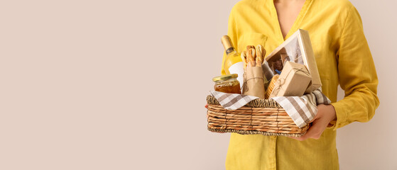 Woman holding gift basket with products on light background with space for text