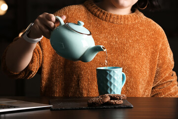 Woman pouring tea into cup at table in cafe, closeup