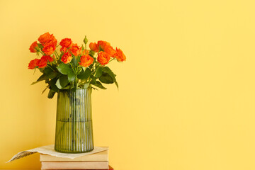 Vase with bouquet of beautiful roses with books on yellow background