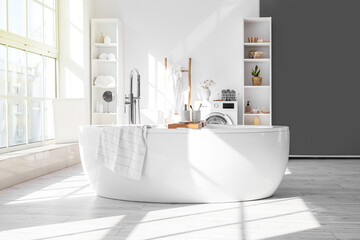 Fototapeta na wymiar Stylish interior of light bathroom with bathtub, shelf units and washing machine