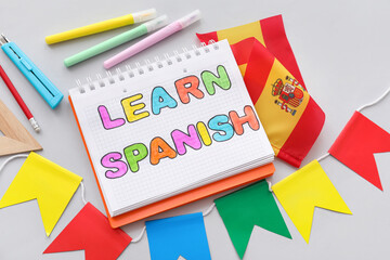 Notebook with text LEARN SPANISH, flag and stationery on grey background