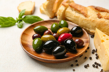 Wooden plate with delicious olives on light background, closeup