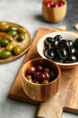 Wooden board with bowls of tasty olives on table, closeup