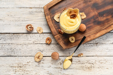 Board with glass bowl of vanilla pudding, walnuts and banana chips on light wooden background