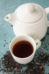 Cup of black tea, teapot and dried leaves on color background, closeup