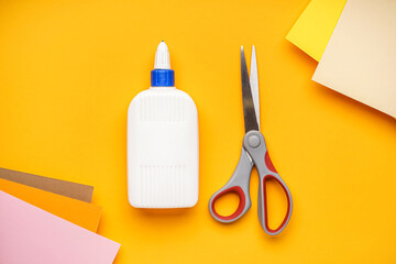 Bottle of glue with scissors on orange background