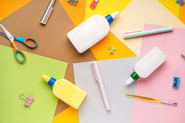 Bottles of glue with stationery and paper sheets on color background