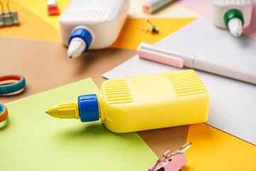 Bottle of glue with paper sheets on color background, closeup