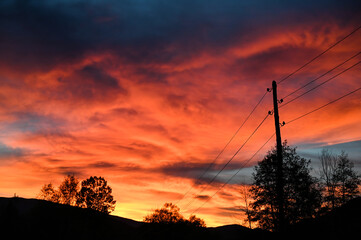 Beautiful orange sunset in summer. Electric poles with power lines at sunset. Electricity transmission.