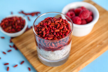 Wooden board with glass of tasty chia seed pudding and barberry on color background, closeup
