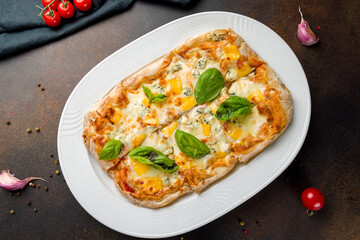 Roman pizza four cheeses on Roman dough, pinsa top view on dark brown table