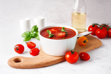 Wooden board with bowl of delicious tomato soup on light background