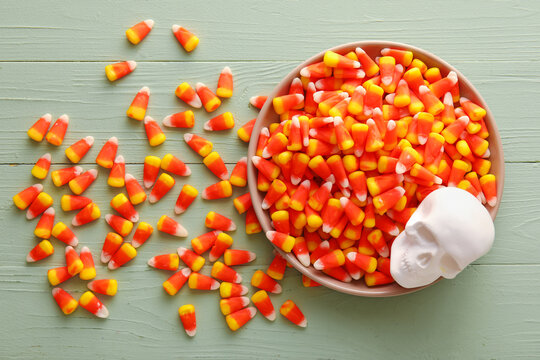 Plate with Halloween candy corns and skull on green wooden background