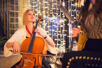Woman playing cello on the concert with her band on the restaurant stage at night © Solid photos