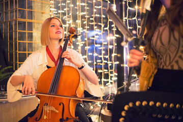 Woman playing cello on the concert with her band on the restaurant stage at night