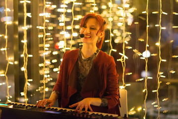 Young smiling woman playing synthesizer in the band on the concert stage in restaurant at night