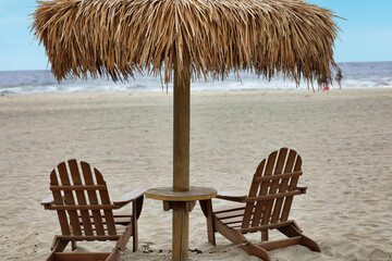 Palapa umbrella and Adirondack chairs on the sand by the ocean.