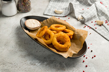 Onion rings in batter with sauce on grey table