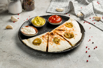 Quesadilla with chicken and sauces on black plate on grey table