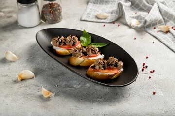 Bruschetta with chicken pate and caramelized onion on black plate on grey table