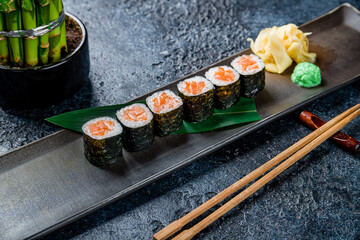 Maki roll with salmon on dark brown plate on dark stone table