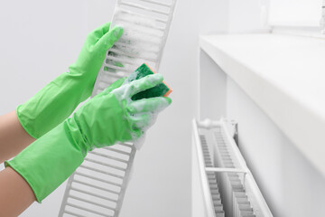 Woman washing radiator grill with sponge and detergent indoors, closeup