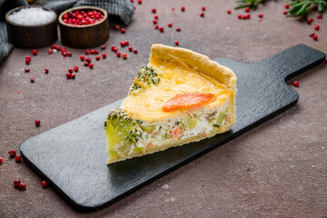 quiche with salmon and spinach on brown table, piece