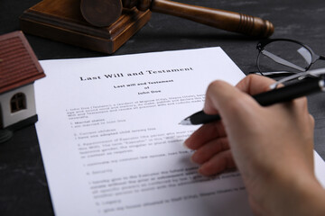 Woman signing last will and testament at black table, closeup - obrazy, fototapety, plakaty