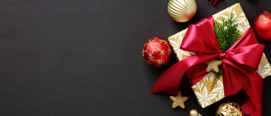 Christmas gift box with red ribbon bow, Xmas ornaments and baubles on black background. Merry Christmas banner design.