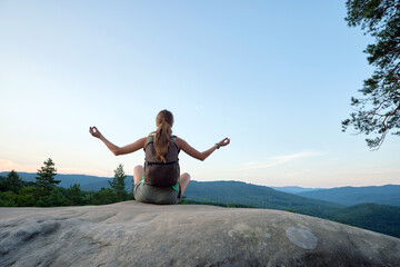 Young woman hiker meditating alone on rocky mountain enjoying view of evening nature on wilderness trail. Active way of life concept