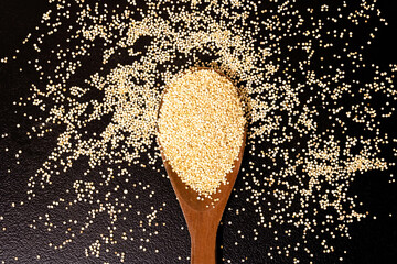 Wooden spoon on a black table with quinoa. Mention healthy eating, natural breakfast with fibers...