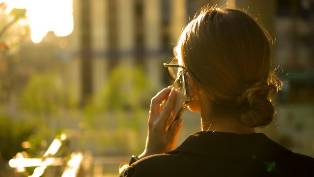 Keep connected and keep your clients happy. Portrait of young businesswoman walking in street talking on smartphone. Caucasian female walks outdoors calling on mobile phone. Back view, slow motion