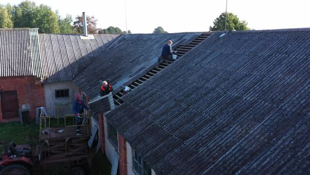 Roofers remove dangerous asbestos slate roof tiles from old building, aerial view