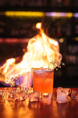 A glass with a cocktail in a nightclub bar. Flames of fire on the background. Night life, club life. Excellent serving of cocktails
