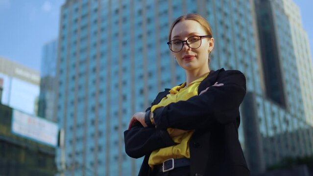 Confident proud young adult businesswoman crossing arms with smile, professional leader, corporate manager, office worker looking at camera at sunset standing at terrace, low angle dolly in