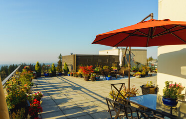 Red umbrella on BC rooftop patio garden with flowers, shrubs, and deck furniture late summer

