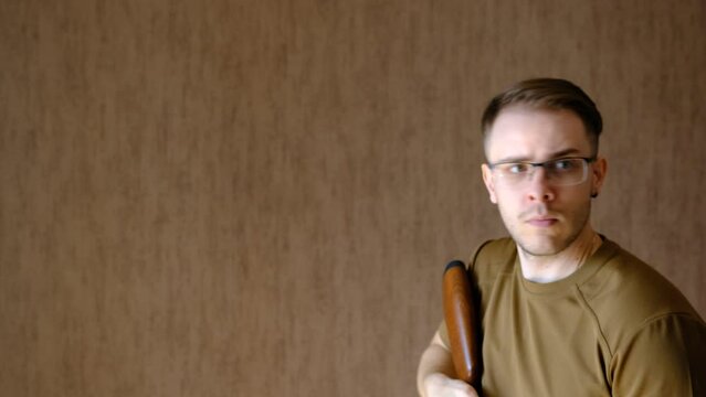 a young man in glasses looks in aim of air gun and look for prey on a brown background. Hunting with air gun. Forward view