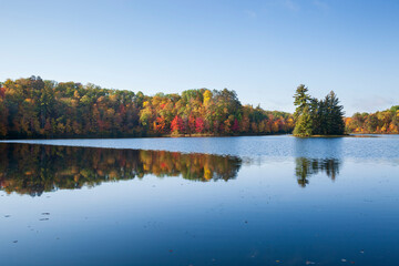 Pretty little blue lake with trees in autumn color and a small island on a bright morning