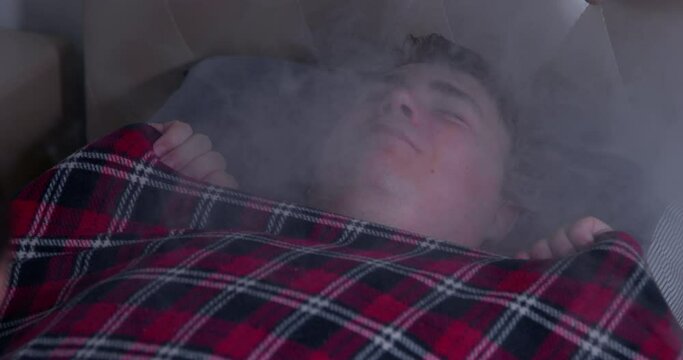 Man lies sleep in bed covered with checkered blanket, snores peacefully in dream, clouds of thick smoke roll over him. False news. Propaganda people, hypnosis, false information absorbs consciousness