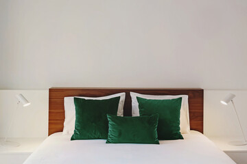 Bedroom in white colors with wooden headboard and green velvet accent pillows