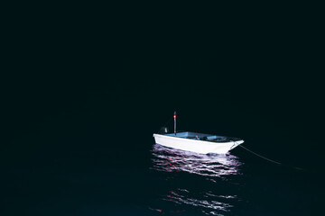 A low-key shot of a small lonely moored boat in the darkness of the night illuminated by a...