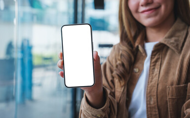 Mockup image of a young woman holding and showing a mobile phone with blank white screen